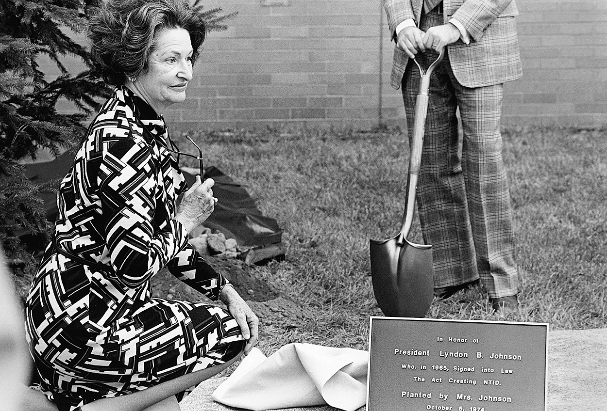First Lady Lady Bird Johnson kneels at the dedication of the LBJ building, 1974