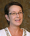 Photo of woman smiling, short dark hair, glasses, white v-neck top with embroidery.