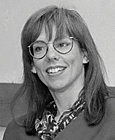 Photo of woman, smiling, long dark hair, glasses, dark suit jacket with patterned scarf tucked into neckline.