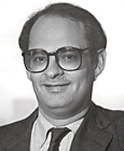 Photo of man, dark hair and glasses, dark suit and tie.