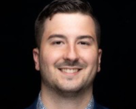 Headshot of young man smiling, dark hair and short hint of mustache and beard