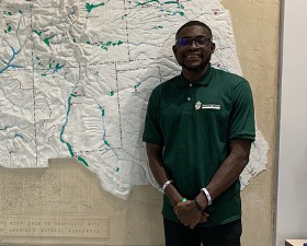 Young dark-skinned man standing in front of map.