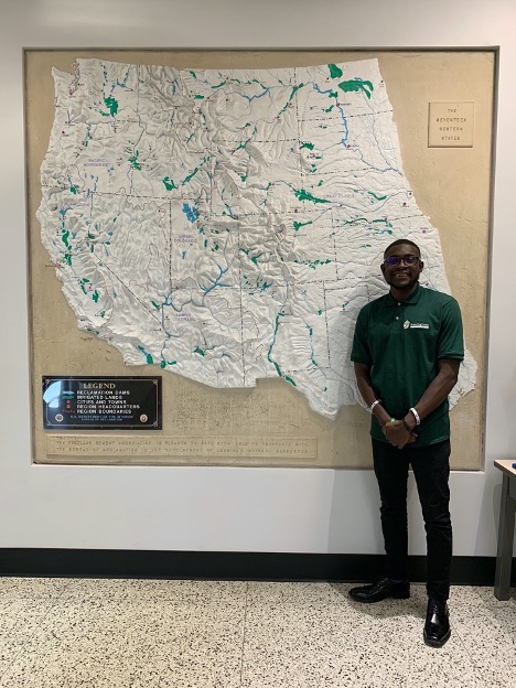 Young dark-skinned man standing in front of map.