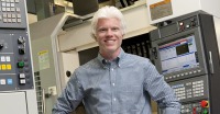 Young man, very light blond short hair, plaid shirt, standing in room of technical monitoring equipment.