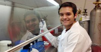 Young man, short dark hair, wearing lab coat, in lab and holding pipette.