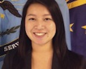 Young woman, dark hair, sitting in front of Defense Finance and Accounting Service banner.