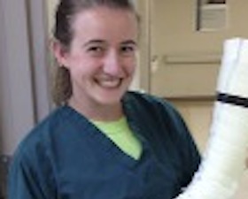 Young woman, brown hair tied back, dark blue medical smock, holding a prosthetic cast.