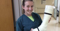 Young woman, brown hair tied back, dark blue medical smock, holding a prosthetic cast.