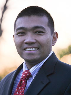 Man with short dark hair, dark suit coat, striped shirt, and red patterned tie.