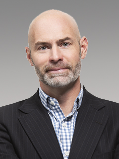 Photo of man, bald, dark suit jacket, striped shirt open at color.