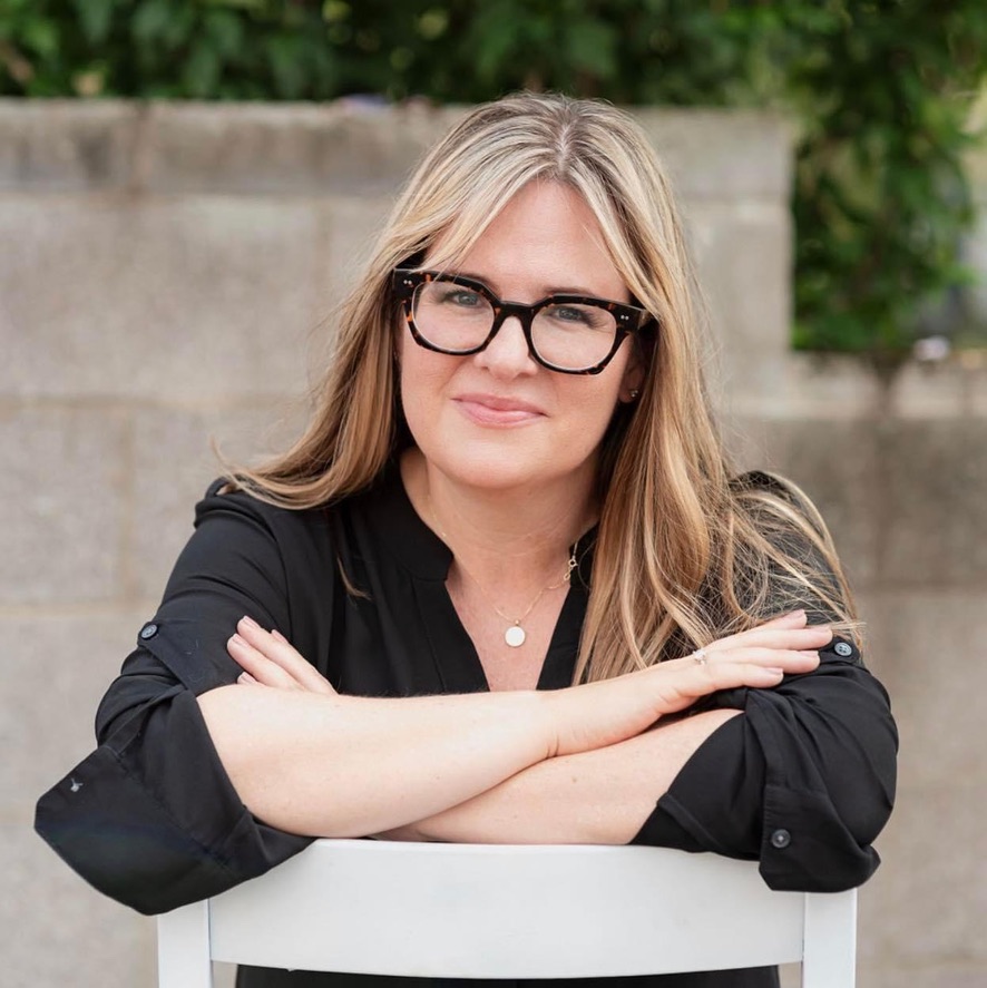 Tera Sumpter, woman with long blond hair, dark glasses, dark blouse, sitting on backward chair with arms crossed over chair back