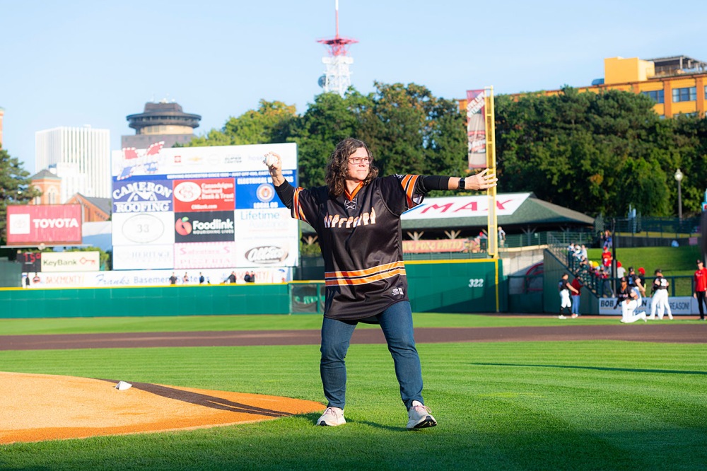Person standing on a baseball field, throwing a pitch.