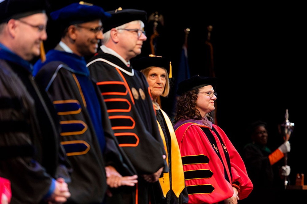 Group of people in academic regalia standing on stage during a ceremony.