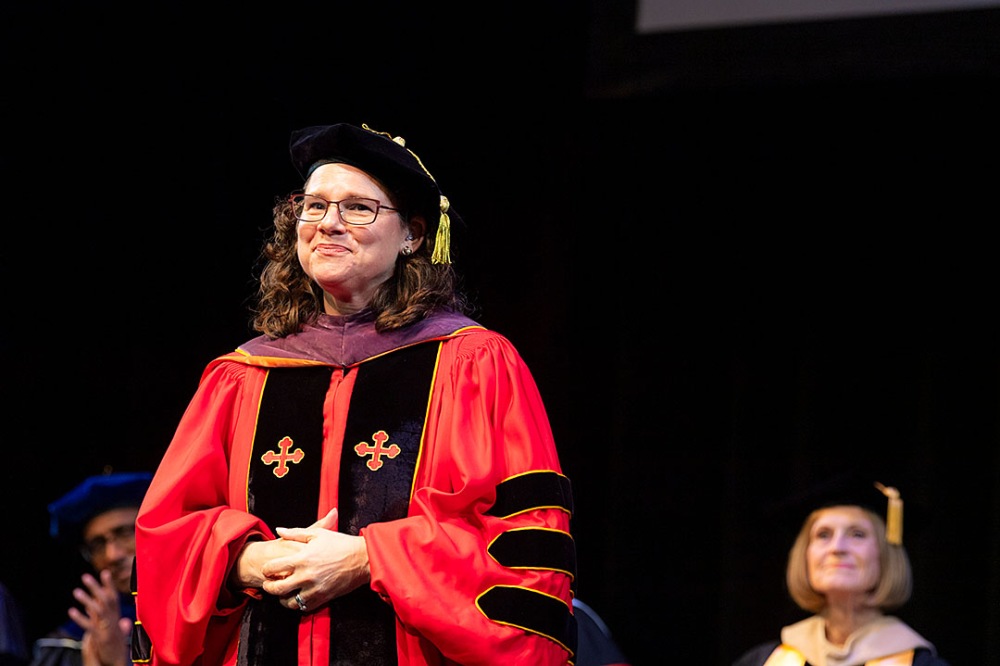 Individual wearing red academic regalia smiling while standing on stage.