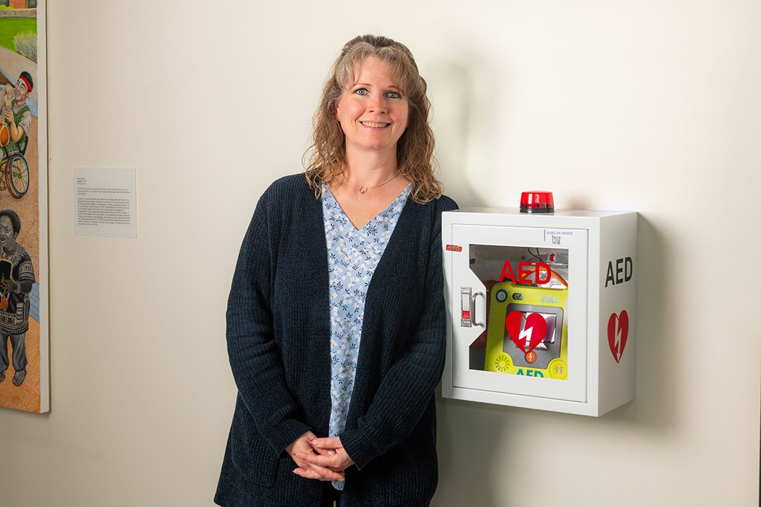 a woman stands next to an A E D device attached to a wall.