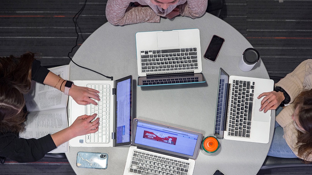Students sitting around a table working on laptops.