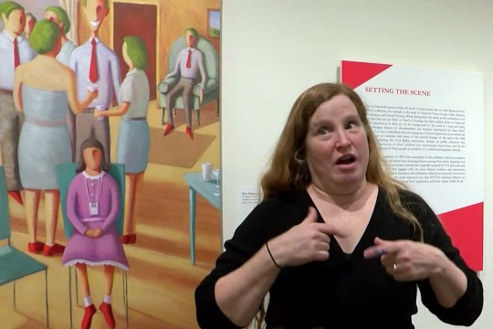 woman signing American Sign Language in front of artwork of a girl sitting alone at a crowd gathers behind her.