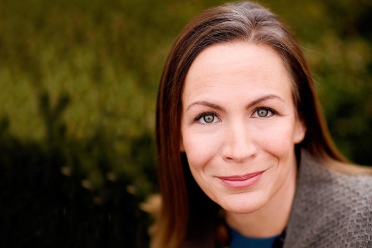 Image of Rachel Coleman with brown hair wearing a blue top, brown sweater and chunky necklace.