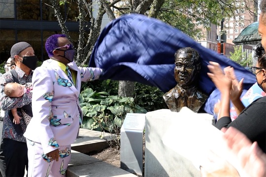 person taking a cloth off of a bust.