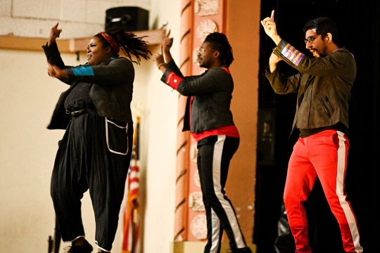 three people of color performing on a stage using American Sign Language.