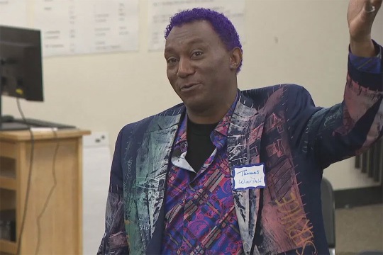 a closeup of Thomas Warfield wearing a purple patterned blazer speaking to students
