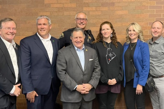Gerald Buckley stands with county and state executives in front of a brick wall.
