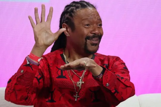 a man in a red shirt signs in A S L while sitting on a white couch.