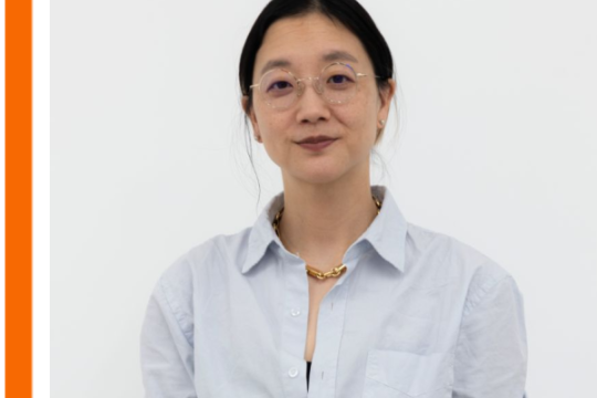 image of Chrstine Sun Kim wearing a light blue shirt and glasses, hair pulled back. She is against a white background. 