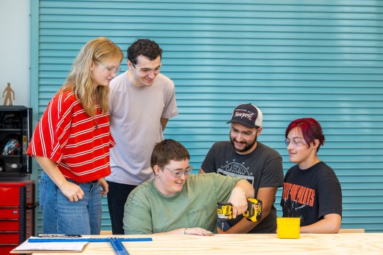 a person offers students an up-close look at some of the set pieces they are building for the upcoming production 