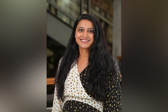 Ashina Singh, a woman with a black long hair and a yellow flower-patterned black and white blouse.