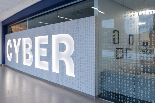 Signage that says "Cyber" in bold white letters is etched on a classroom's glass window with white numbers in the background..