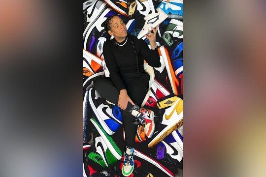 Ebony Watson poses, holding a sneaker in her hand. She is superimposed over a background of colorful Nike sneakers.