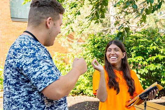 photo of students smiling and signing on campus on a sunny day