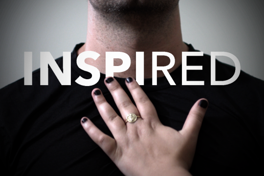 A hand with fingers spread, palm facing a person's chest with a text overlay that reads "Inspired"