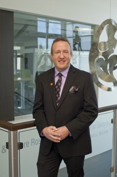 Light skinned male wearing dark suit and tie standing in front of glass display case.