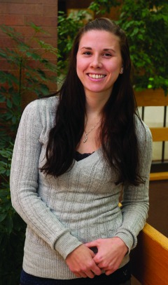 Light skinned young woman with long dark hair wearing v-neck sweater leaning elbow on railing.