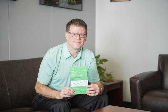 Light skinned person wearing light green golf shirt holding a green book.