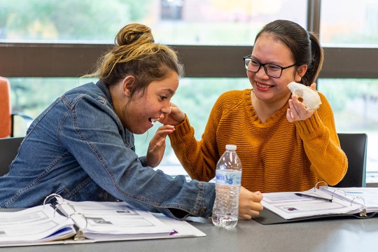 two students working side by side at a table.