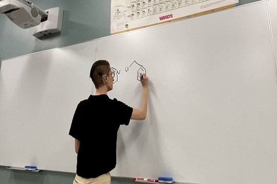 college student with a cochlear implant writing on a dry erase board.