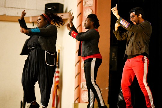 three people of color performing on a stage using American Sign Language.