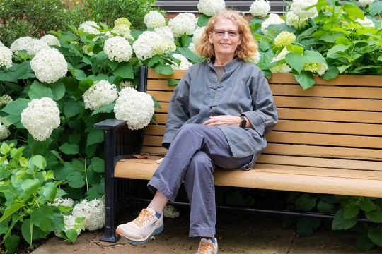 woman sitting on a park bench next to large white flowers.