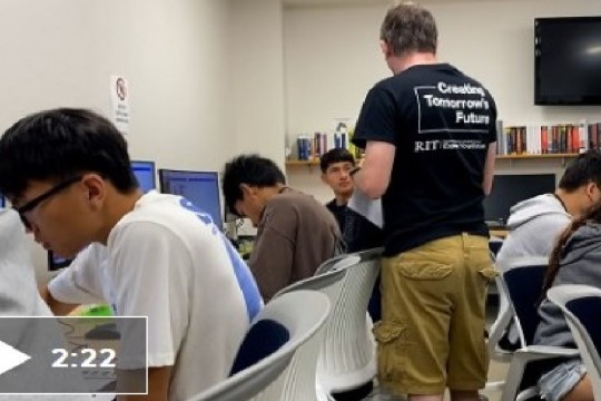 Six kids sitting at computers. One camp counselor standing.
