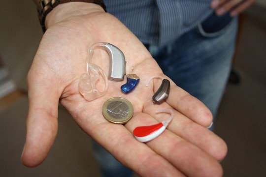 person holding four types of hearing aids and a coin in his hand.
