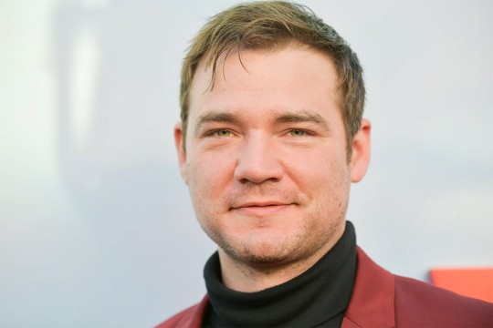 daniel durant looks at the camera wearing a red suit jacket and black turtleneck.