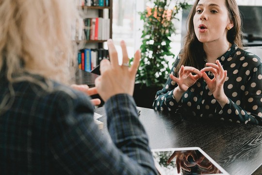 two women speaking in ASL at a table in a coffee shop