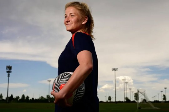 Mia White stands in profile on a soccer field holding a soccer ball.