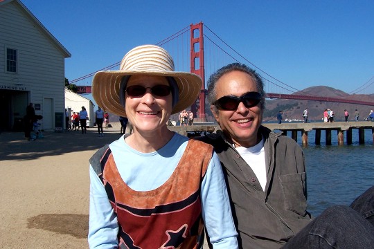 a man and woman sit smiling for a photo in front of the golden gate bridge,