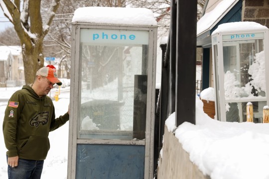 A man stands by an old phonebooth on a snowy street