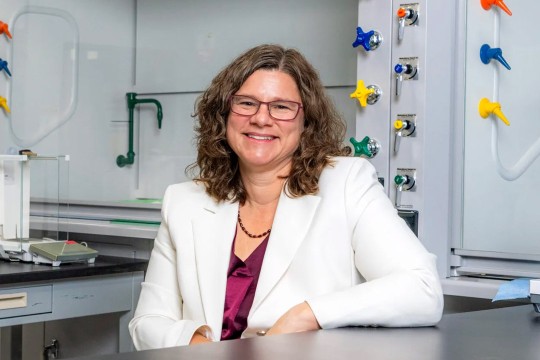 a woman with curly hair sits leaning against a table.