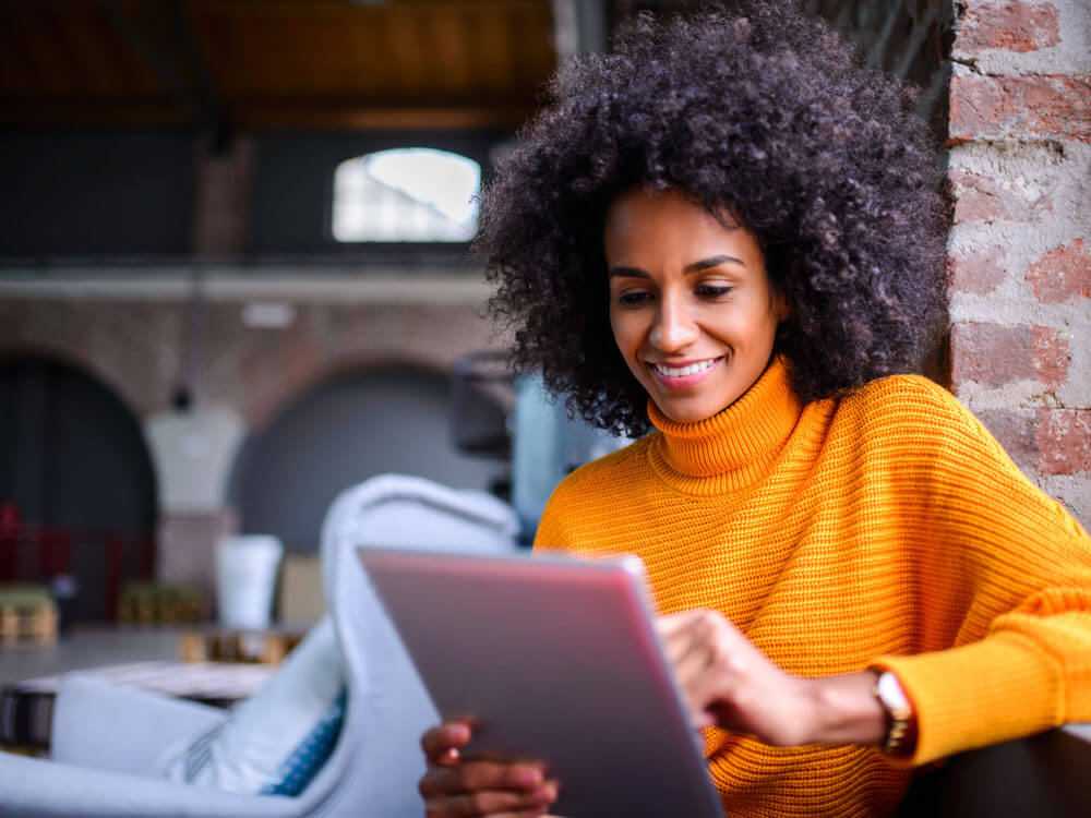 A female student wearing an orange sweater works on a tablet.